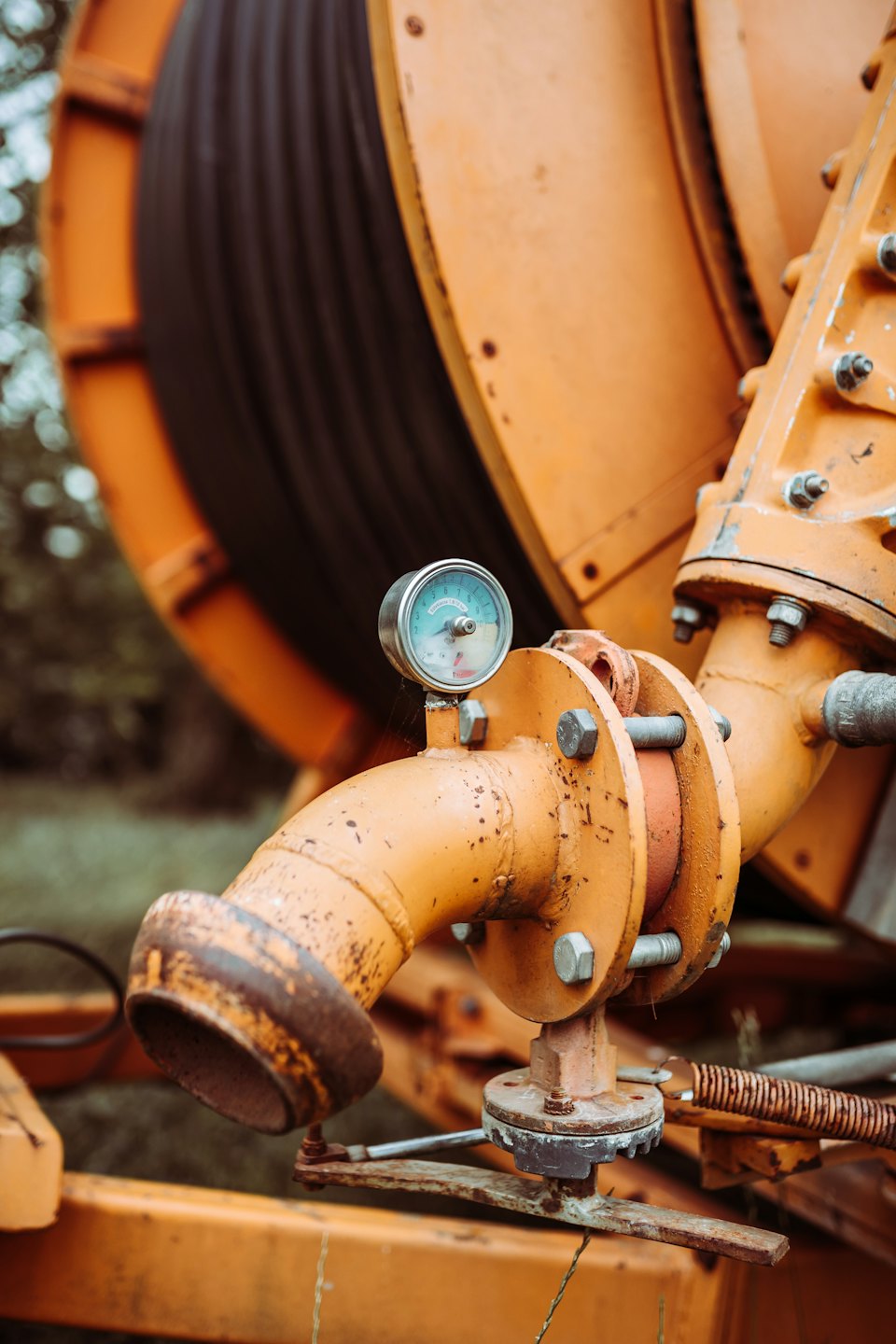 Weathered orange industrial pipe with pressure gauge on farm machinery.